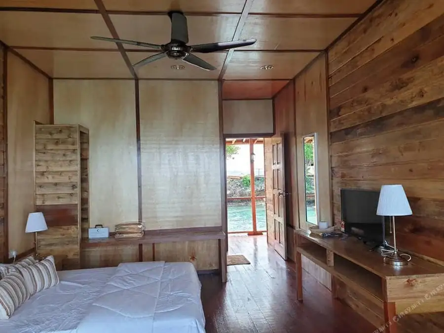 A classic bedroom at Dreamy Wave Dwelling Resort with a bed facing an open door to the ocean, rustic timber walls with smooth wooden boards, and air conditioning.