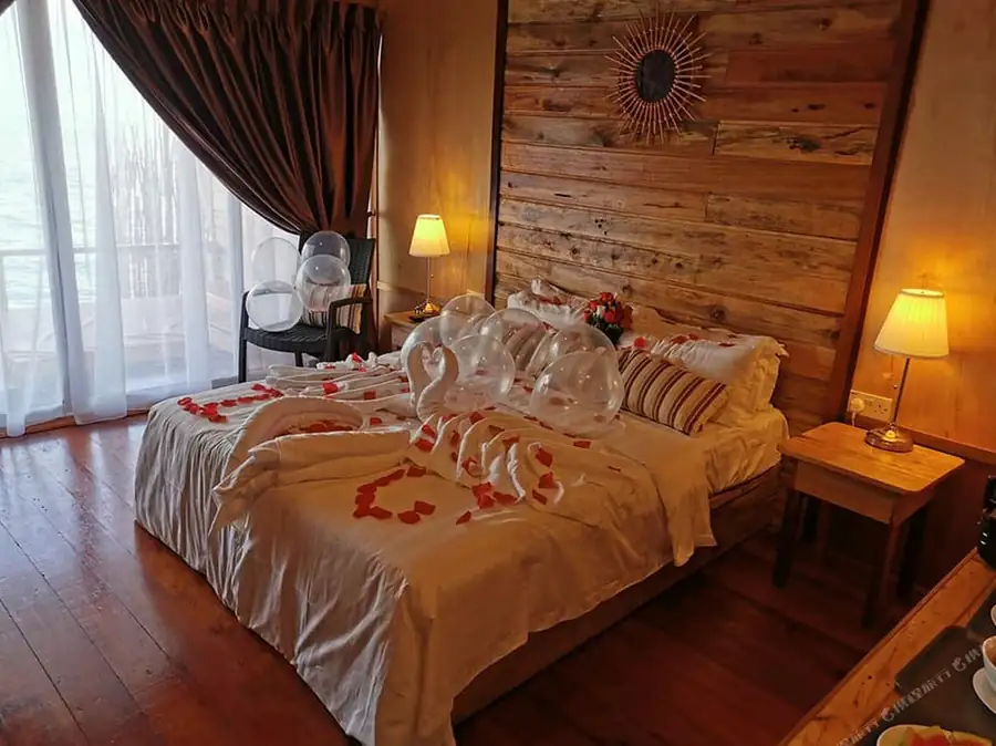 A bedroom at Dreamy Wave Dwelling Resort near Pulau Bum Bum featuring swan towels, floor to ceiling glass doors, traditional Sabahan style wood paneling with gleaming timber floors, and AC.